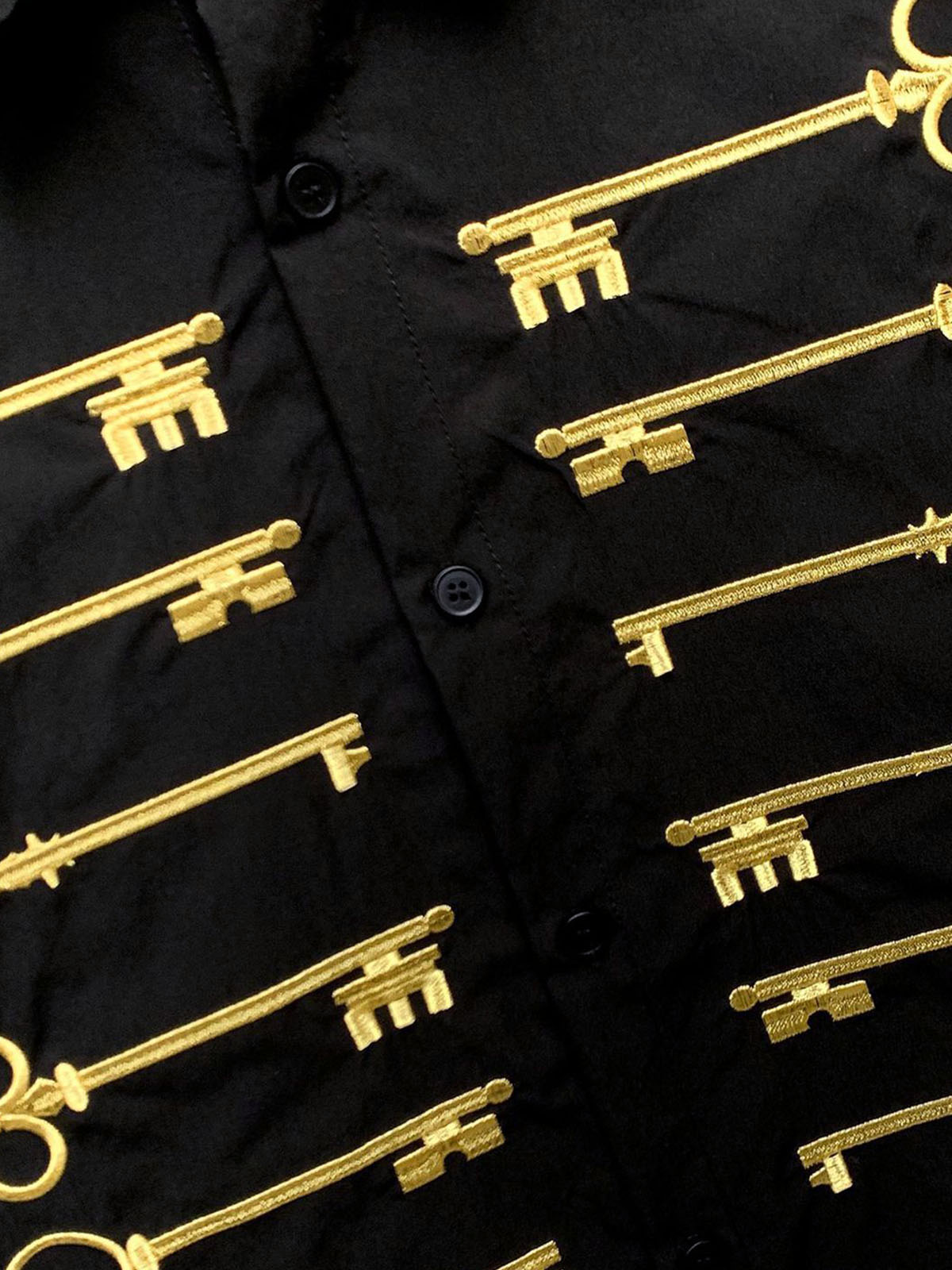 Camisa negra de algodón con botones y motivo de llave bordado en dorado.