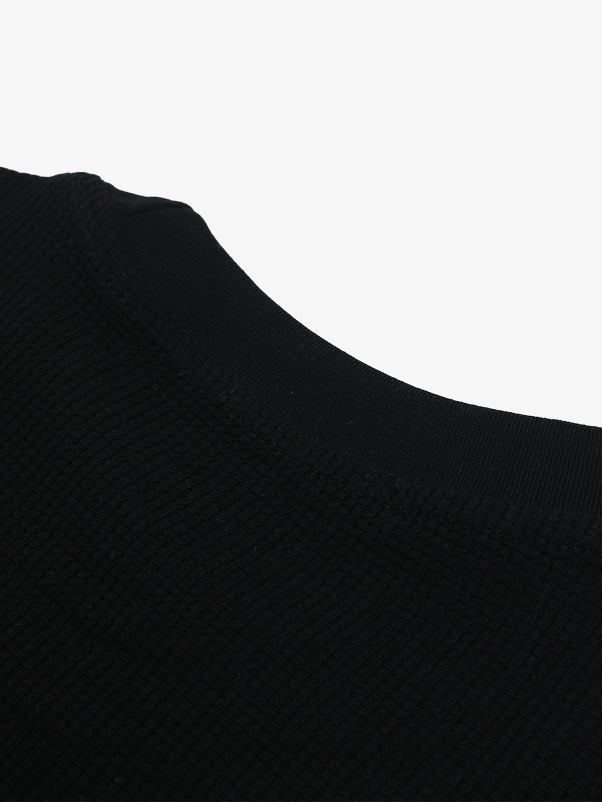 Close-up of black waffle-knit T-shirt fabric showing the raised grid texture around the collar