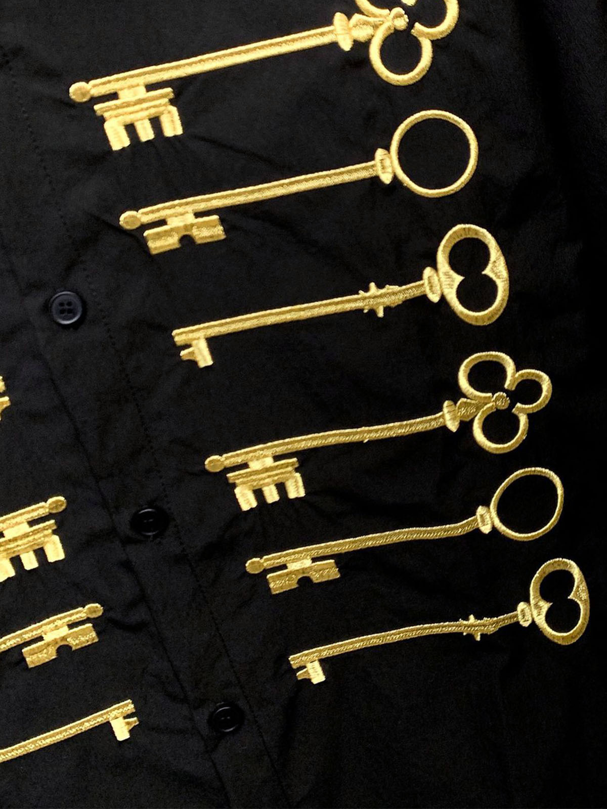 Camisa negra de algodón con botones y motivo de llave bordado en dorado.
