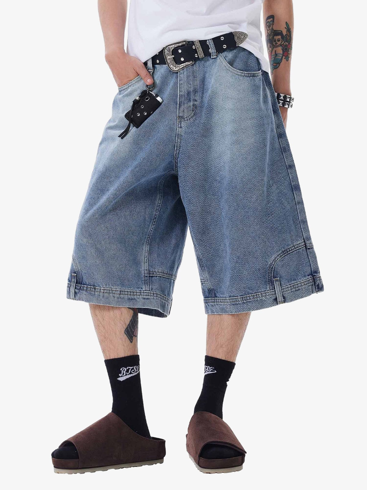 Person wearing blue denim shorts with a belt and black socks on a white background