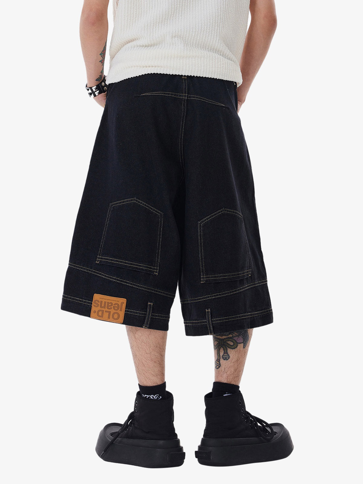 Person wearing black denim shorts with a visible brand label on a white background