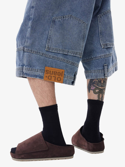 Person wearing blue jeans with a brand label, black socks, and brown shoes on a white background